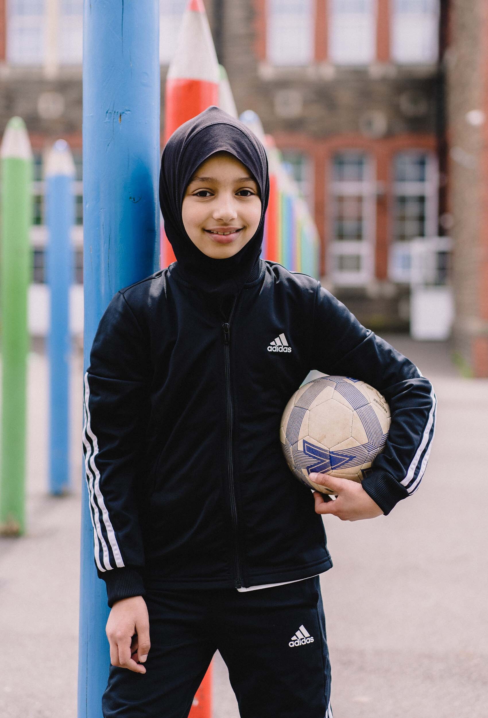 a young girl smiling, holding a football in her primary school courtyard