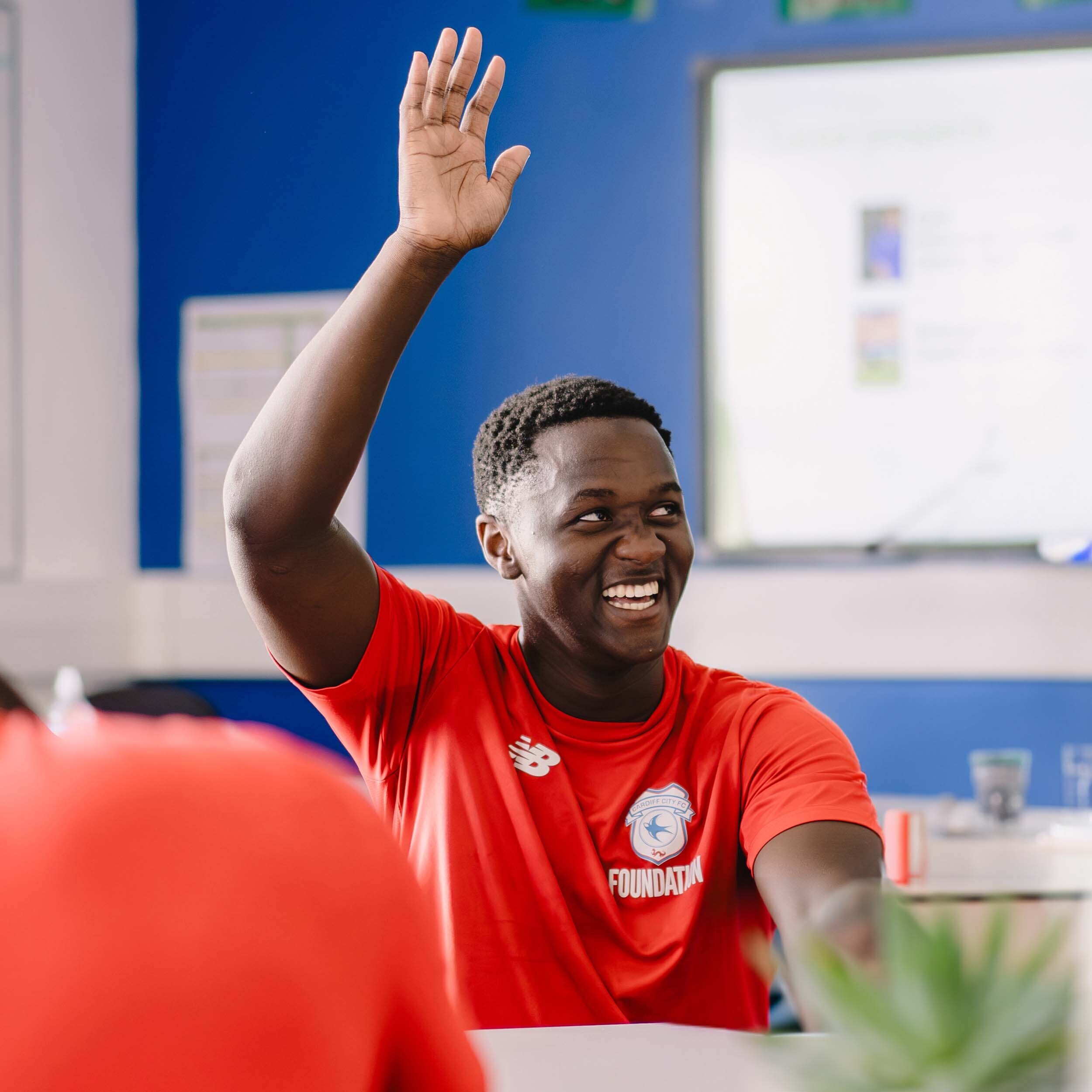 a young black male raising his hand smiling in a school classroom