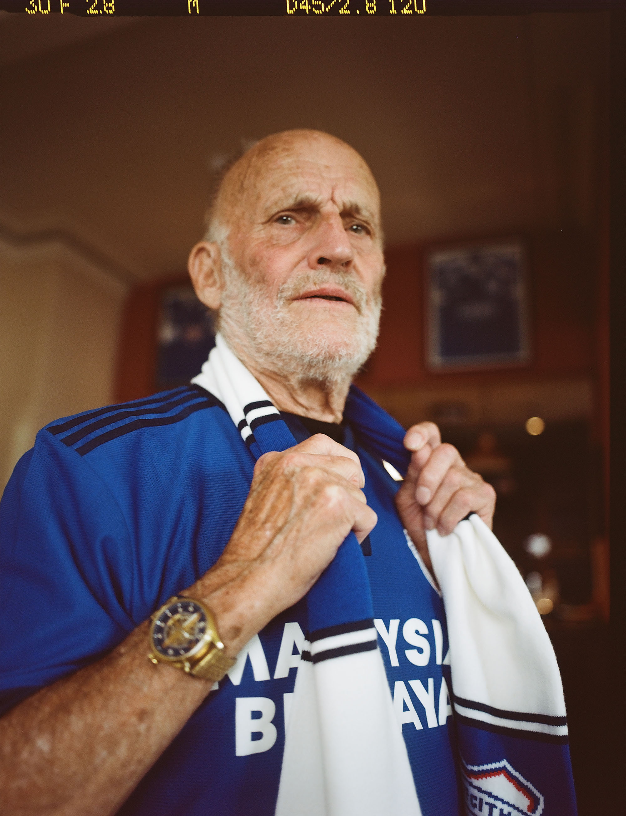 An older man wearing the 2021/2022 Cardiff City Football Club home shirt with a matching scarf.
