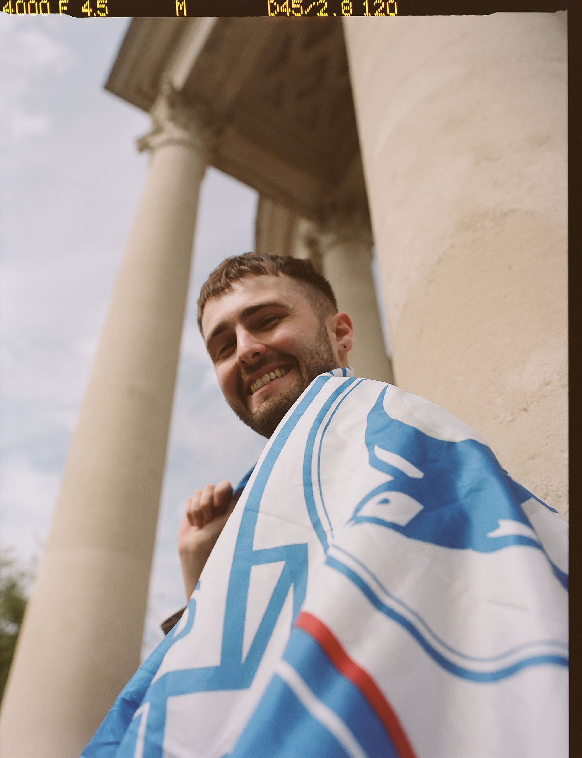 A man with a flag draped over his shoulders. The flag shows the Cardiff City Football Club crest.